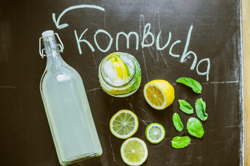 Foto colorida. Imagem mostra uma garrafa contendo um líquido branco e vários limões ao redor. A palavra Kombucha está escrita de giz - Metrópoles