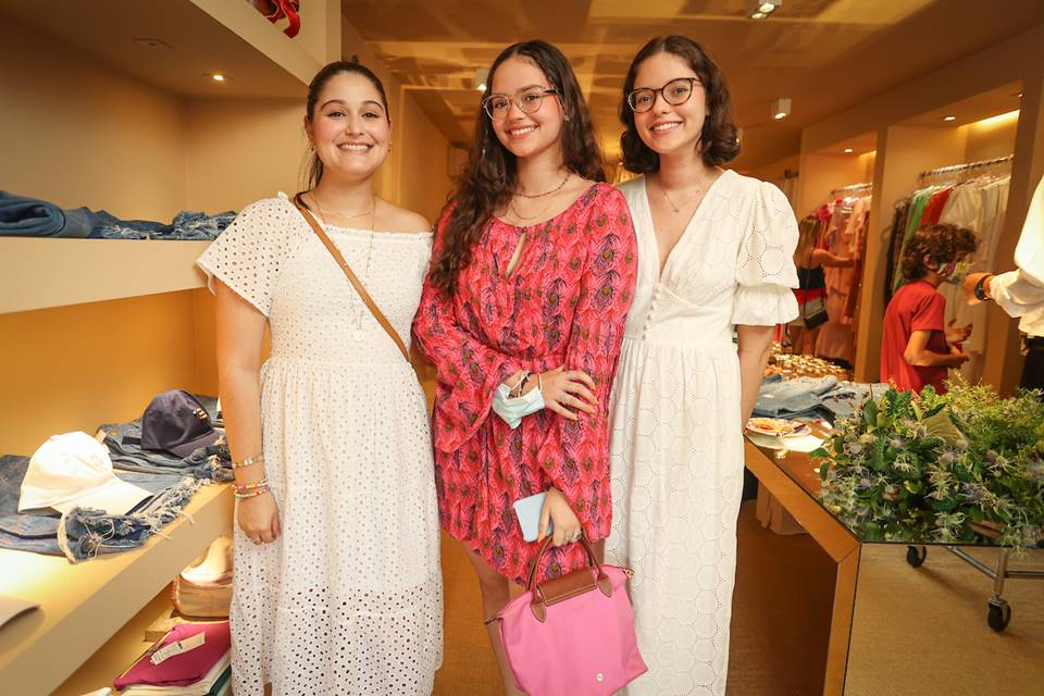 Três mulheres juntas em um ambiente de loja de roupas 