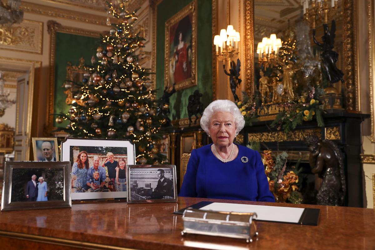 Mulher sentada ao redor de porta-retratos. Quadros e uma árvore de Natal aparece ao fundo