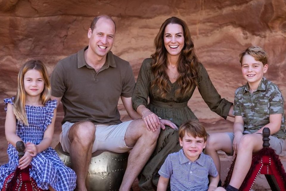 Homem e mulher ao lado de três crianças sentadas. Dois meninos e uma menina. A família parece estar em uma gruta