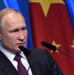 Sob fundo azul com parte da bandeira da China, o presidente russo Vladimir Putin fala em evento. Dois microfones estão posicionados a sua frente - Metrópoles