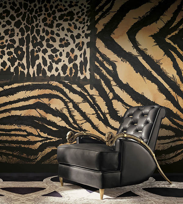 Poltrona preta com ferragens douradas em um sala com papel de parede de zebra. Há ainda, na imagem, um quadro que imita a pele de uma onça. Toda a decoração é da marca Roberto Cavalli.