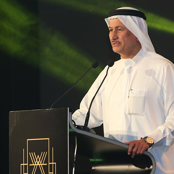 Homem de pele clara com vestes típicas dos Emirados Árabes. Ele está em um palanque com um microfone agradecendo ao recebimento de um prêmio.