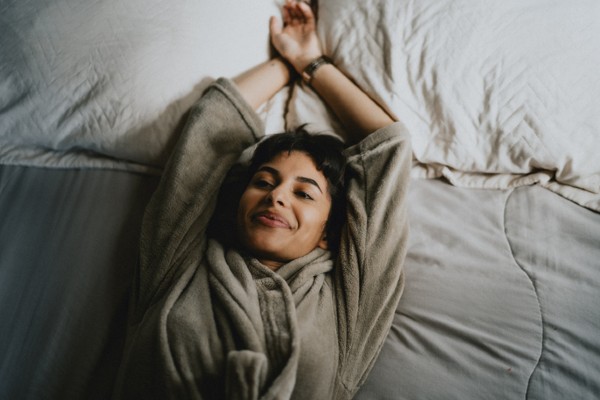 Mulher deitada em cama se espreguiça com os braços para cima-Metrópoles