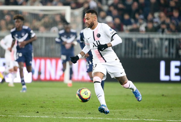 Neymar Júnior, jogador brasileiro de futebol. Ele tem cabelos escuros, usa uniforme de time de futebol e olha seriamente para a frente enquanto corre atrás da bola de futebol - Metrópoles