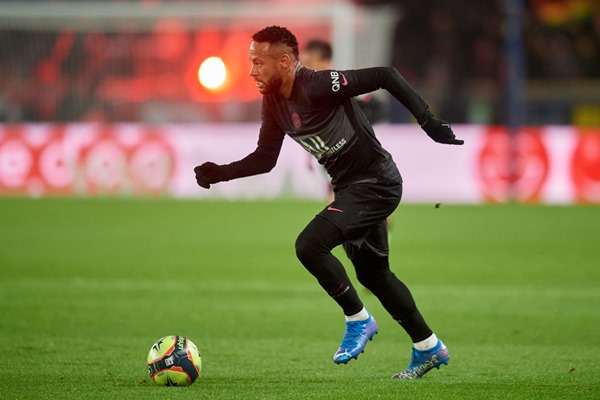 Neymar Júnior, jogador brasileiro de futebol. Ele tem cabelos escuros, usa uniforme de time de futebol e olha seriamente para a frente enquanto corre atrás da bola de futebol - Metrópoles