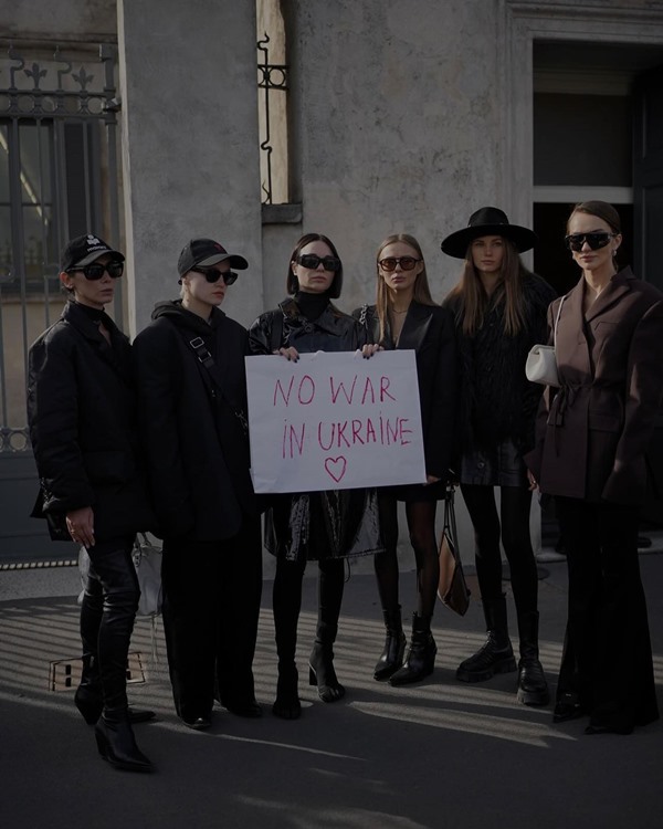 Pessoas brancas em roupas pretas segurando um cartaz que pede o fim da guerra na Ucrânia