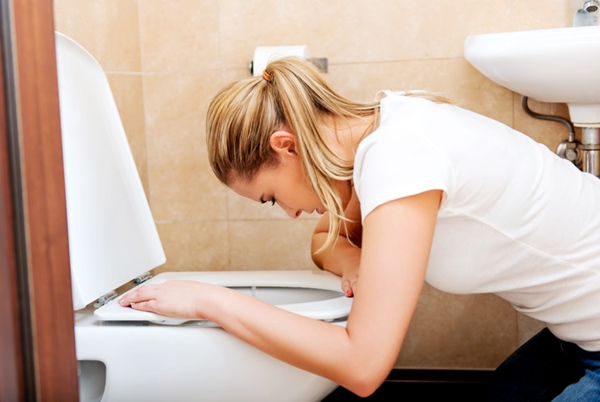 Frau schaut in die Toilette, als ob sie sich übergeben müsste - Metropolen