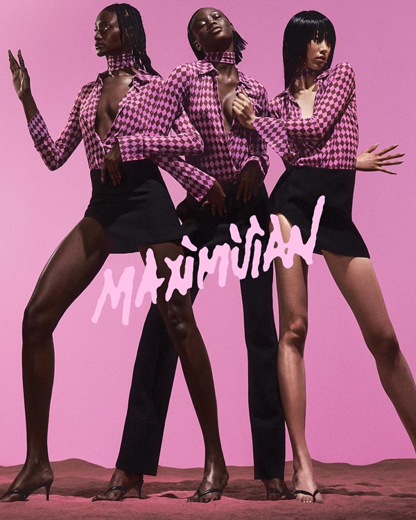 Três mulheres posam em foto de campanha para a marca Maximilian Davis. As duas primeiras são mulheres negras e a terceira é asiárica. Ela usam saias e calças pretas e camisas abertas com uma estampa quadriculada rosa. 