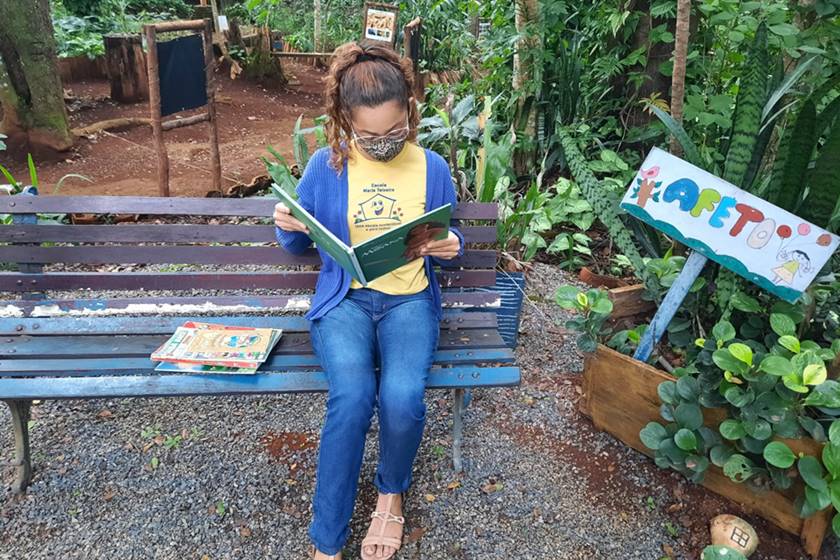 Foto colorida. Mulher lê um livro sentada em um banco