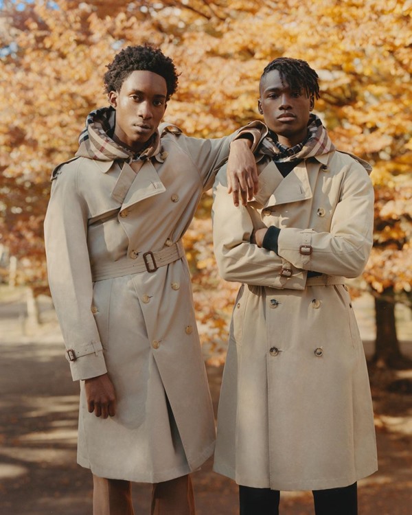 Dois homens negros em campanha da marca Burberry. Os dois usam o trenchcoat - ou sobretudo - da marca, em tom bege, e com cachecol xadrez. 