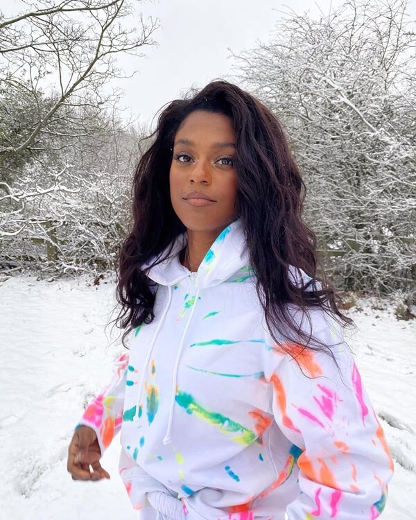 Na imagem com cor, mulher negra no fundo da neve com casaco