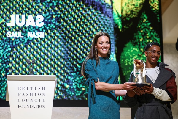 A duquesa Kate Middleton, com um vestido azul turquesa, entregando um prêmio para o estilista Saul Nash. O evento é organizado pelo órgão de moda British Fashion Council.