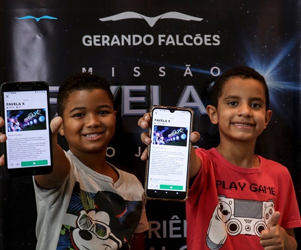 Dois meninos negros, com cabelos curtos, segurando um celular e mostrando o jogo Favela X, desenvolvido pela ONG Gerando Falcões, e patrocinado pela Havaianas