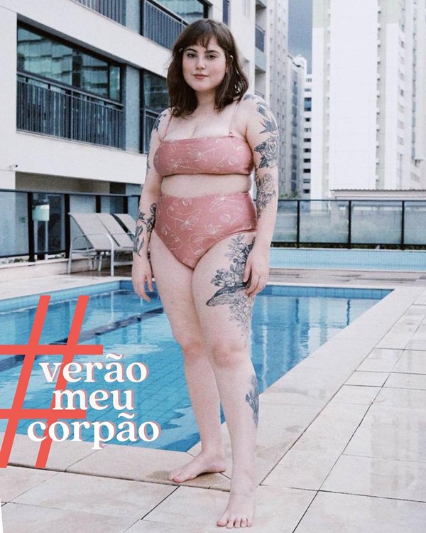 A influenciadora digital brasiliense Nanna Fernandes, uma mulher branca, jovem, com cabelos lisos e com tatuagens pelo corpo. Ela está posando para foto na beira da piscina e usa um biquíni rosa claro com desenhos brancos.