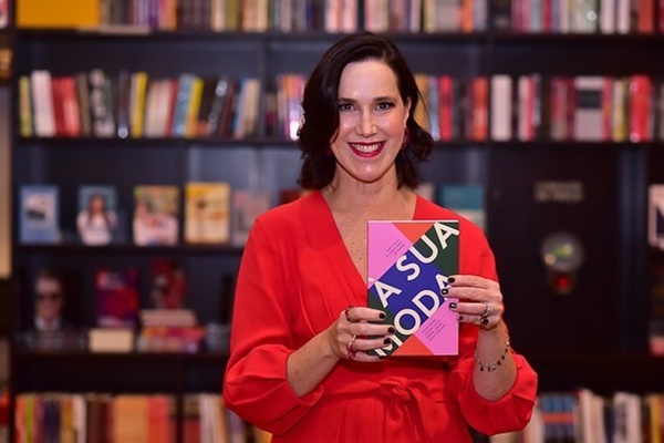 A consultora de estilo Rachel Jordan, uma mulher de meia idade branca, de cabelo ondulado curto, posando em uma livraria com o livro de sua autoria na mão. Ela usa um vestido vermelho