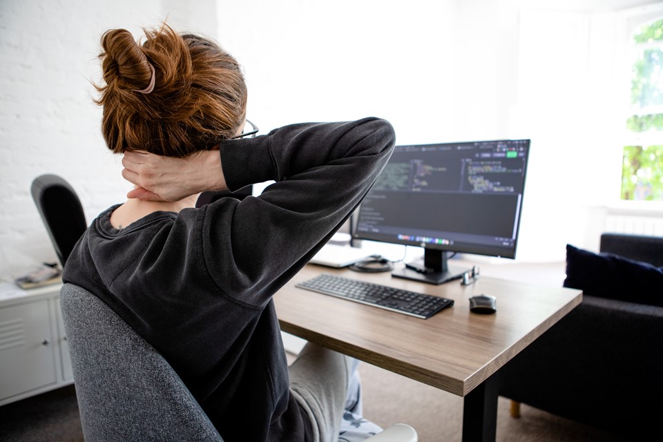 Mulher sentada em frente ao computador com mão no pescoço - Metrópoles
