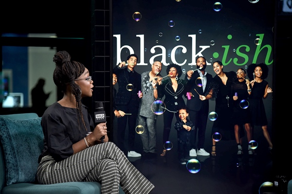 A atriz Marsai Martin, uma mulher jovem e negra, de cabelos trançados, em um programa de TV falando sobre a série Black-ish