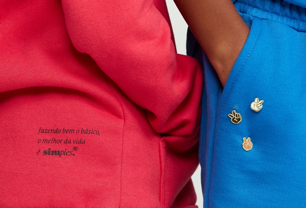 Campanha de divulgação da Simples, submarca da Reserva, onde modelos posam com as roupas em um fundo branco. Na foto, é possível ver detalhes dos casacos de moletons nas cores azul e vermelho.