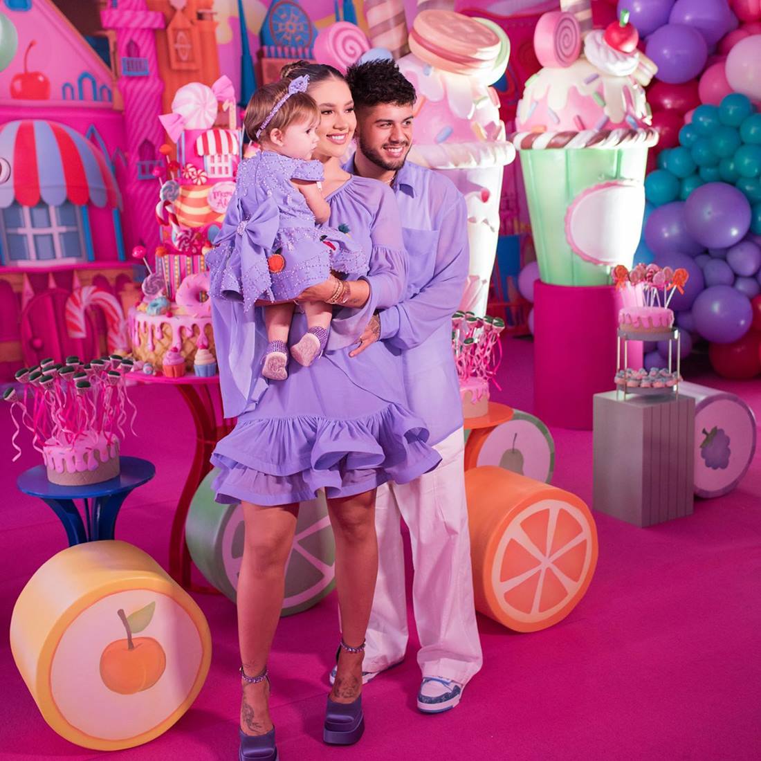 Virginia Fonseca Costa, o marido Zé Felipe e a filha Maria Alice. Todos usam roupas na cor lilás e, ao fundo, está o cenário da festa de aniversário da criança. - Metrópoles