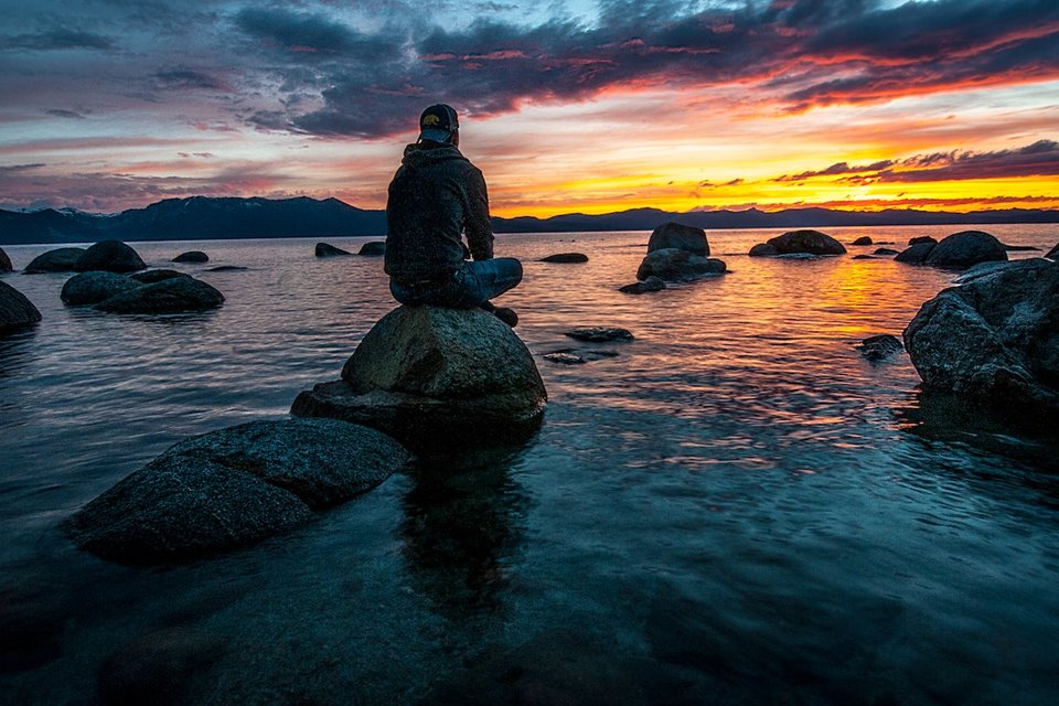 Homem de costas sentado em pedra em meio a uma paisagem cercada por água - Metrópoles