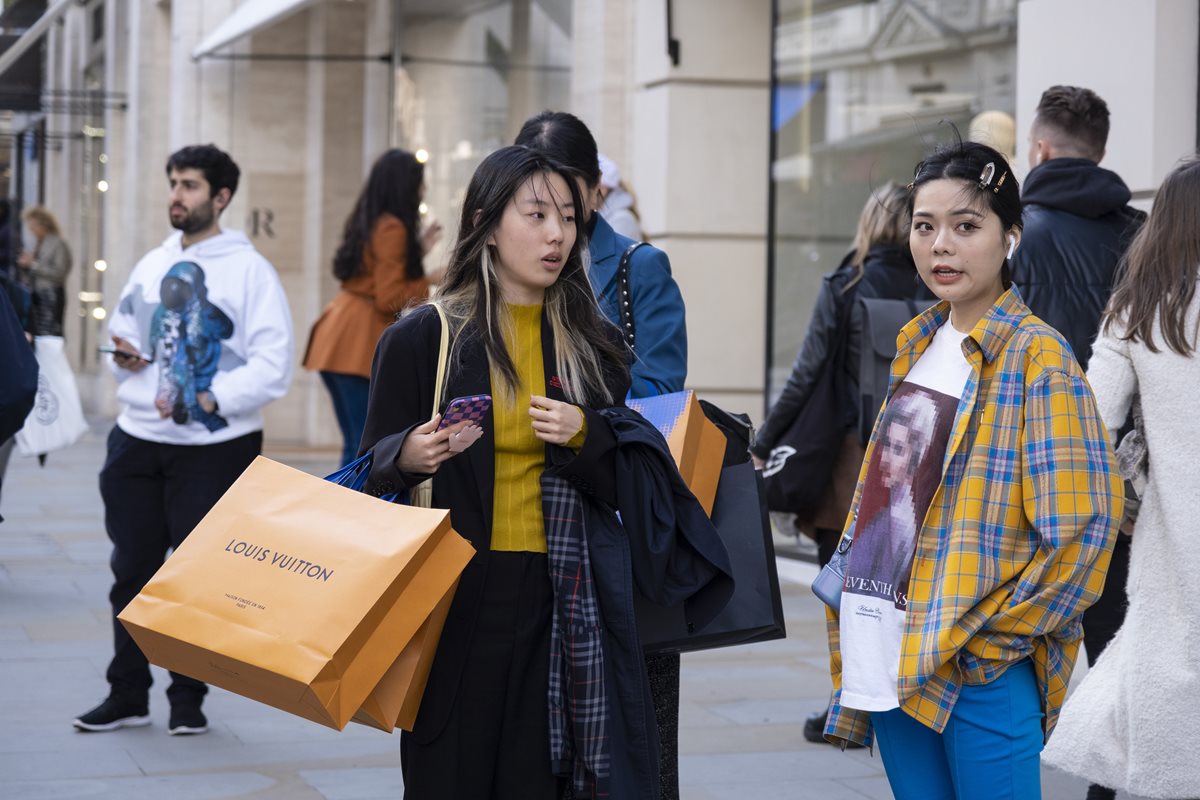 Duas meninas jovens e asiáticas andando pelas ruas de Londres, na Inglaterra. Elas são brancas e possuem os cabelos lisos e longos e seguram sacolas de compras com a logomarca da grife Louis Vuitton. - Metrópoles