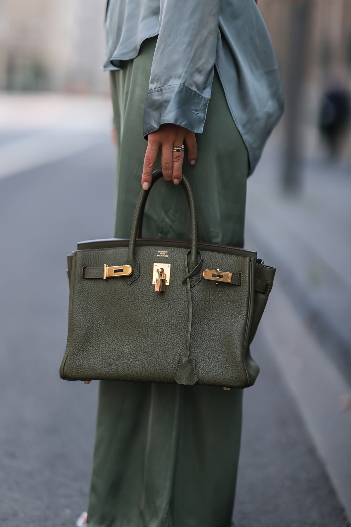 Bolsa Birkin, da marca Hermès, na cor verde musgo. Uma mulher branca segura a bolsa. Na foto é possível ver apenas sua mão. - Metrópoles