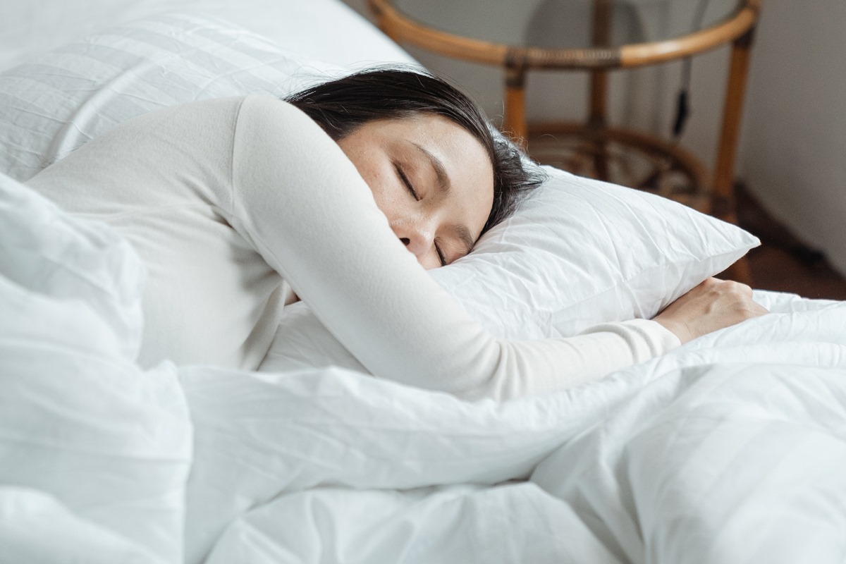 Mulher asiática dormindo em uma cama - Metrópoles