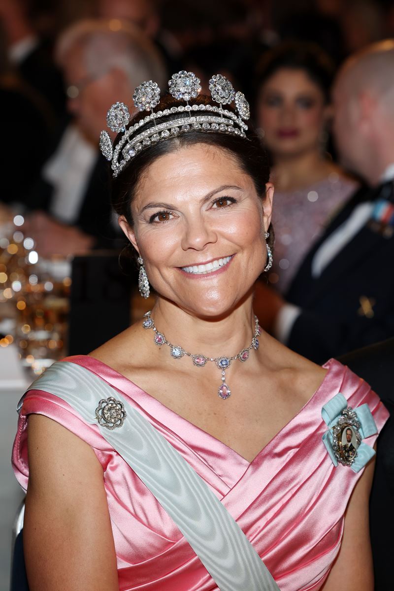 Foto colorida de mulher parda, sorridente, com tiara de pedras preciosas e roupa de gala - Metrópoles