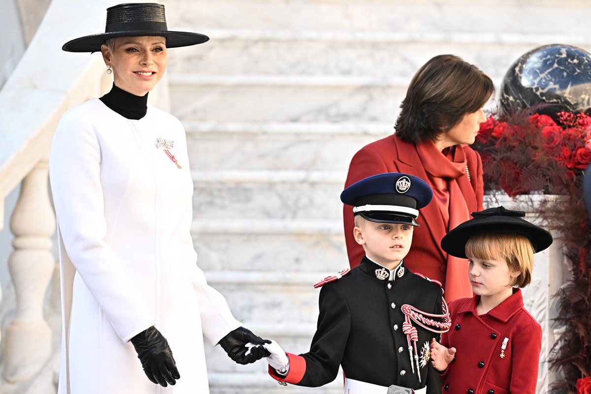 Foto colorida de mulher branca, com chapéu preto e roupa branca de mãos dadas com menino branco com roupas militares e uma menina branca com uma roupa na tonalidade vermelha - Metrópoles