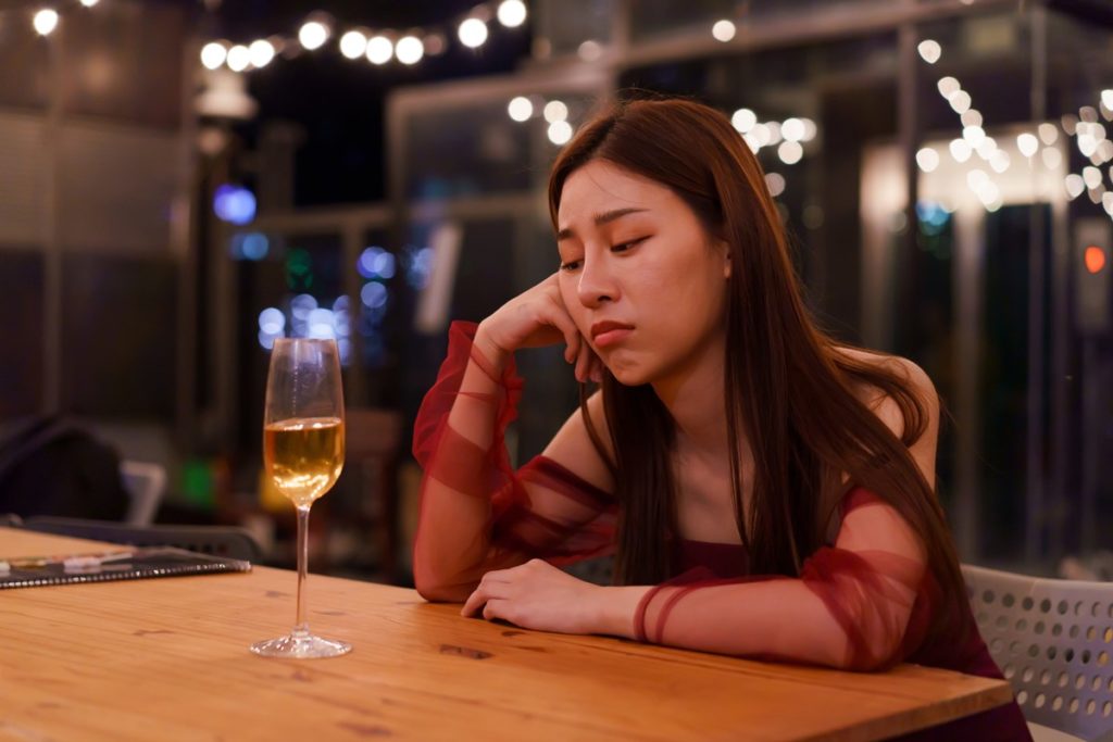 mulher asiatica, branca, com cabelos pretos e lisos está triste olhando para uma taça de champanhe - Metrópoles