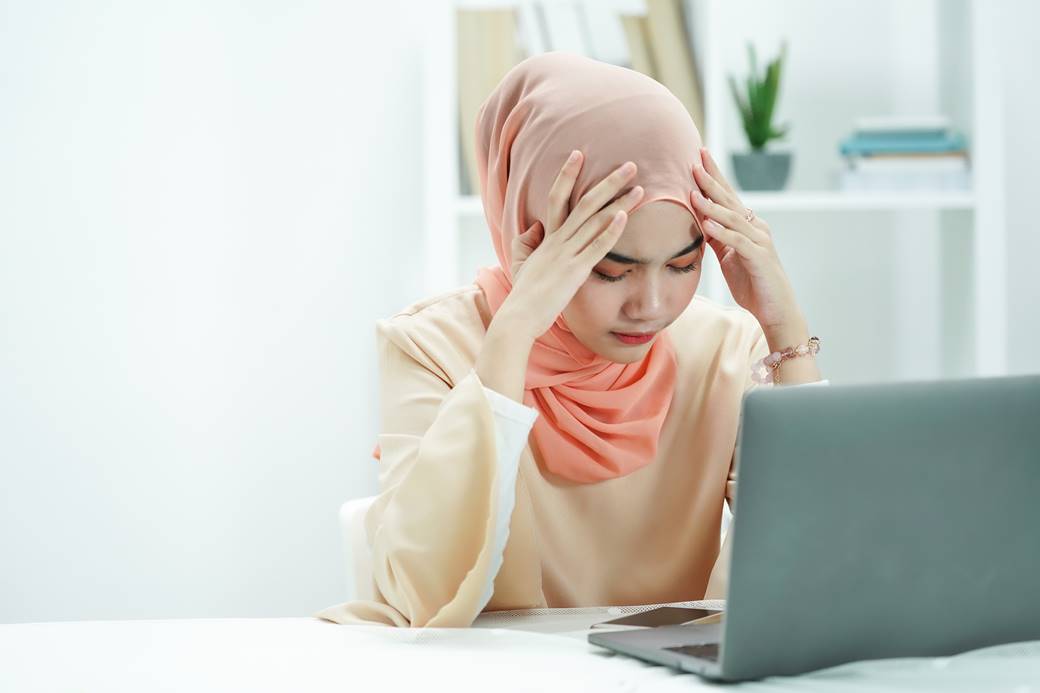 mulher branca com de turbante olhando para o computador com as mãos na cabeça
