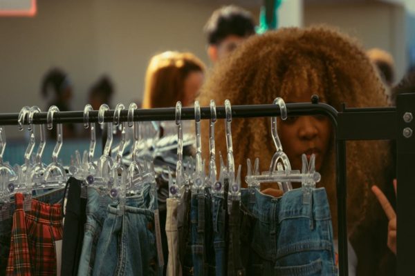Na imagem com cor, uma mulher negra de cabelos cacheados em frente a uma arara de roupa - Metrópoles