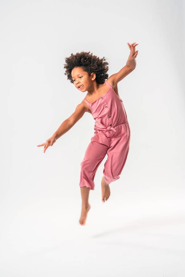Criança pulando para foto em fundo branco. Ela está com os braços abertos - Metrópoles