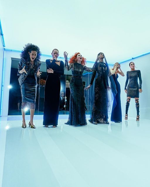 Na imagem com cor, seis mulheres em pé com vestidos pretos em um fundo azul - Metrópoles