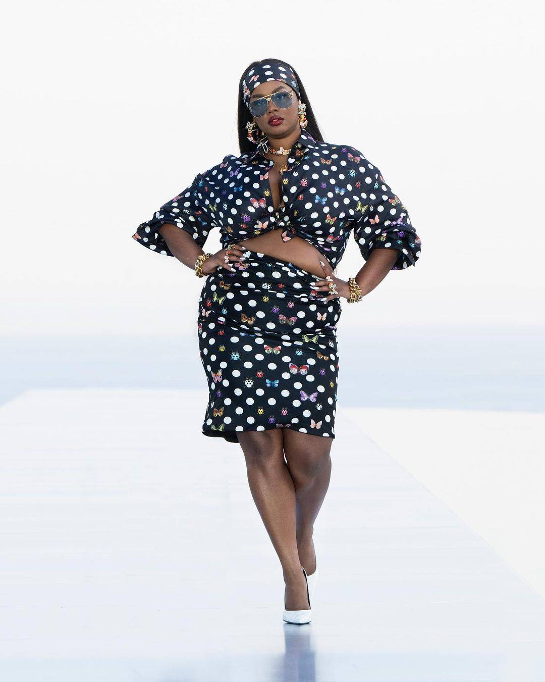 Na imagem com cor, uma mulher negra gorda usando um conjunto de cropped e saia com a estampa de poá - Metrópoles