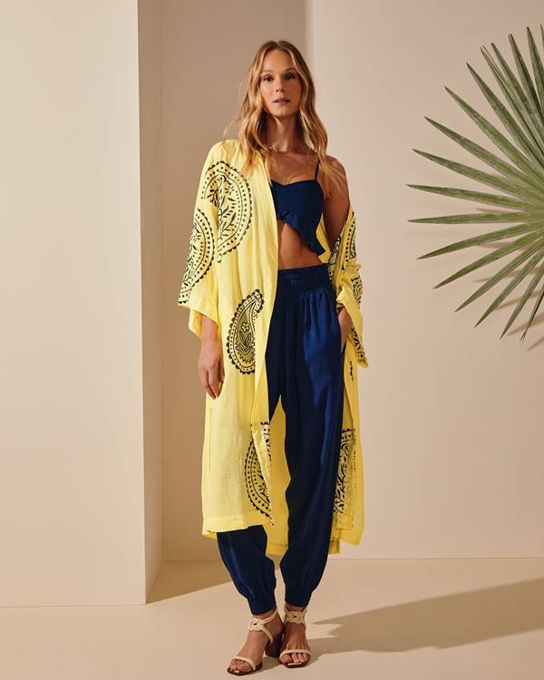 Modelo loira usando look azul com calça e cropped, além de quimono amarelo - Metrópoles
