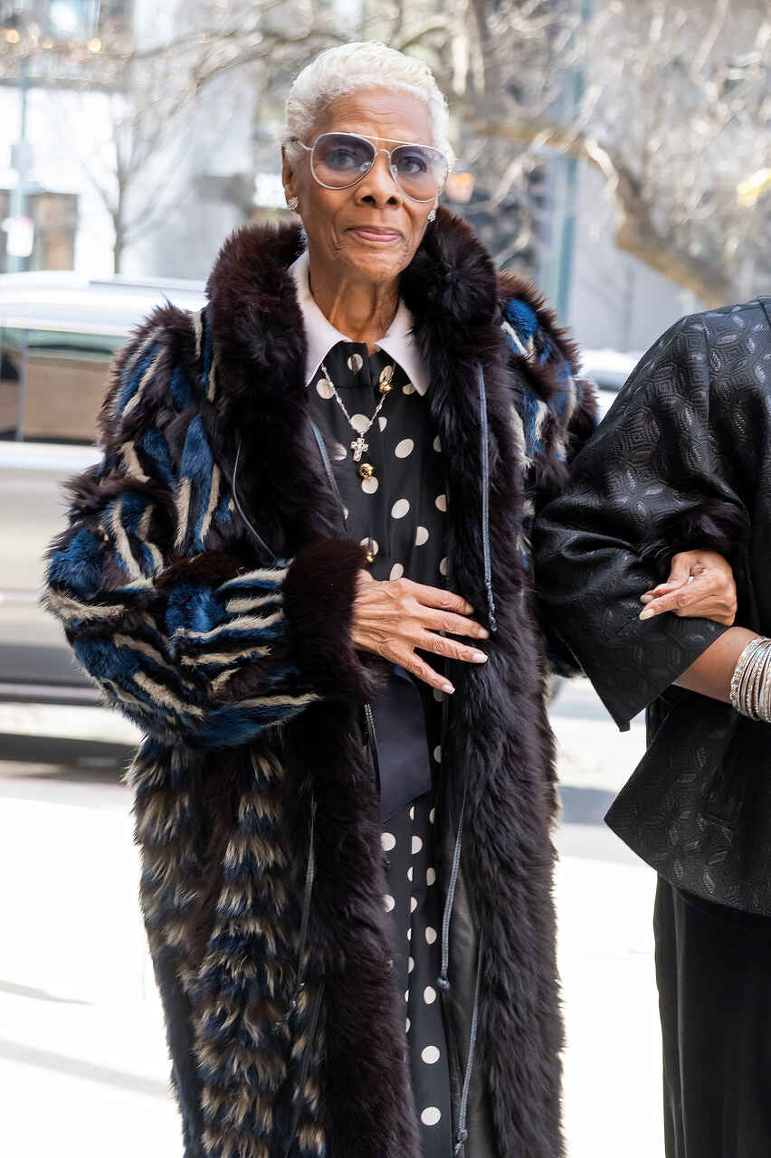 Na imagem com cor, uma mulher negra mais velha usando um casaco e andando - Metrópoles