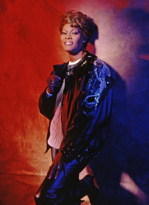 Na imagem com cor, uma mulher negra encostada em uma parede posando com uma jaqueta - Metrópoles