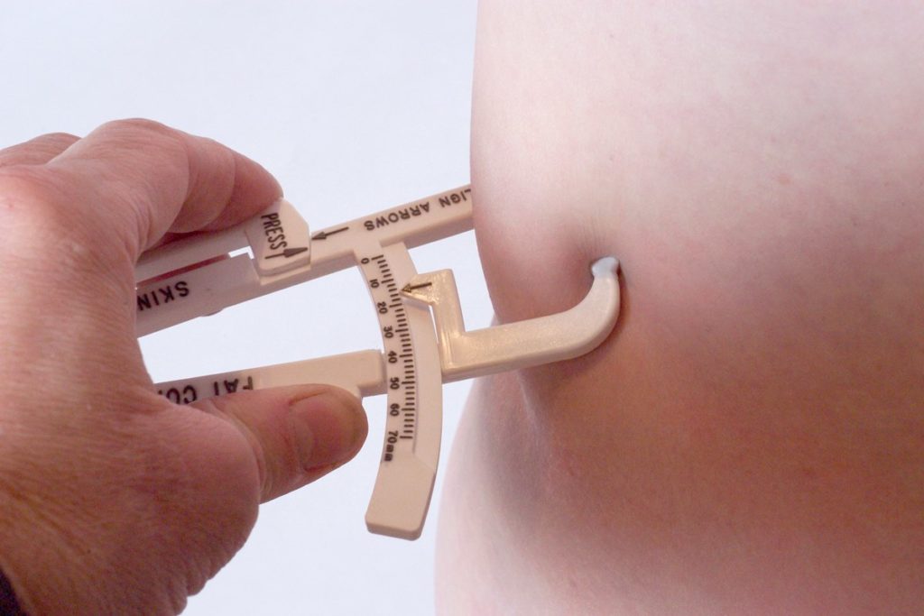 Foto colorida de mão segurando uma pinça de medir gordura abdominal - Metrópoles