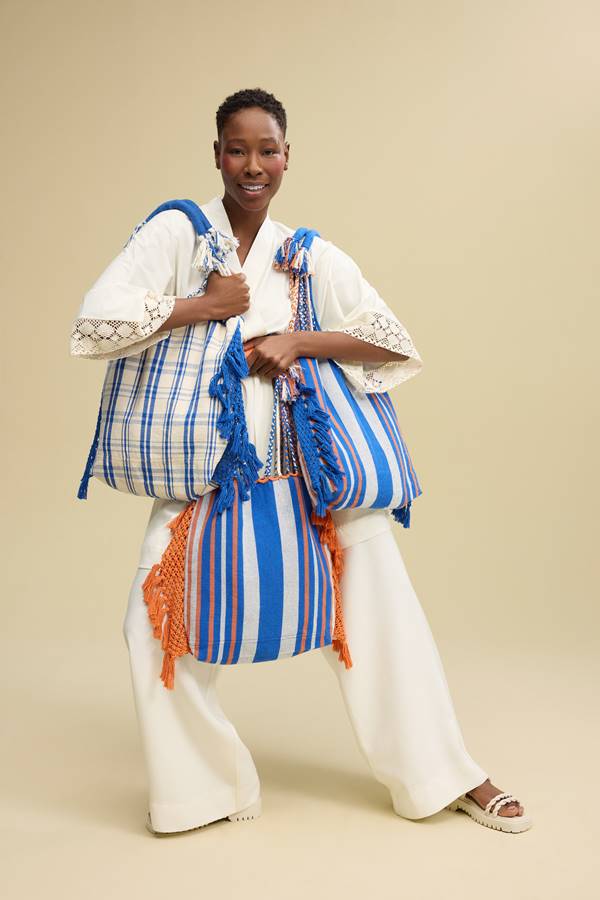 Modelo usa look branco e segura bolsas coloridas com destaque para o azul - Metrópoles