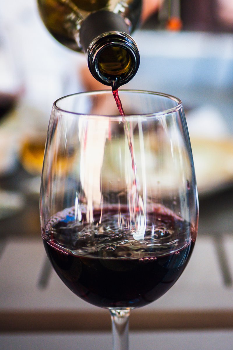Foto colorida de vinho, dentro de uma garrafa, sendo colocado em uma taça - Metrópoles