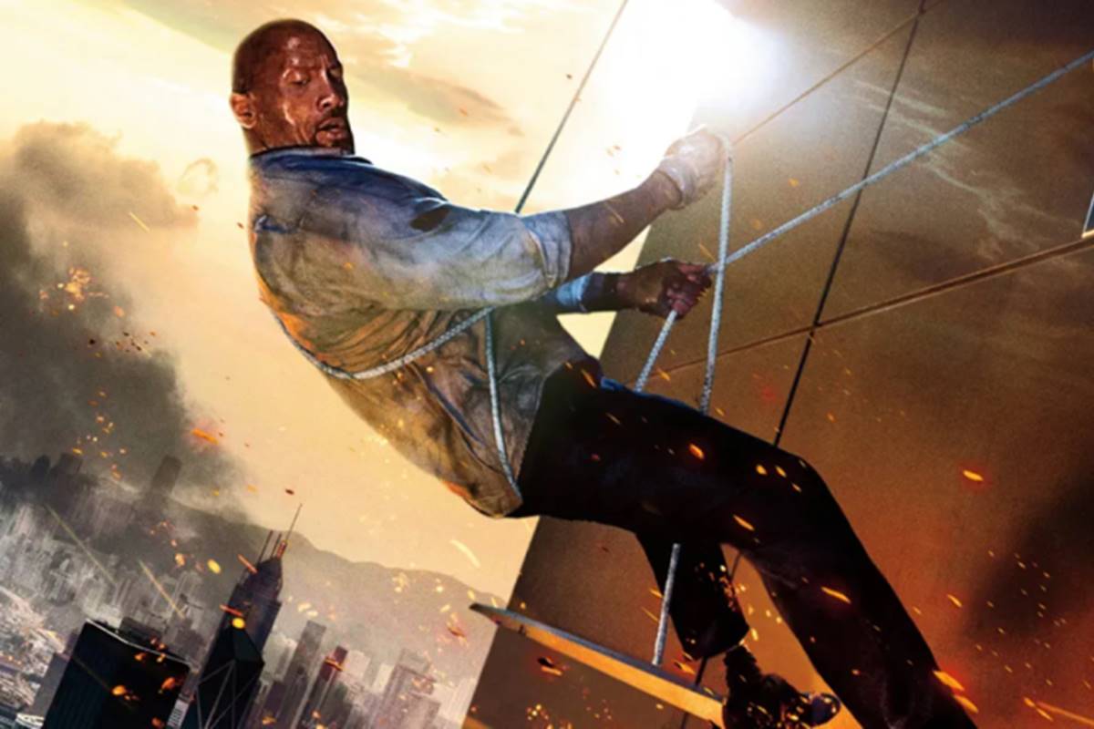 Imagem colorida do ator Dwayne Johnson no alto de um arranha-céu sendo segurado por uma corda. Cena do filme Arranha-Céu - Metrópoles 
