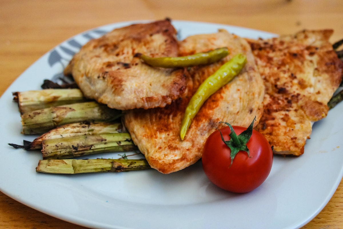 Fatias de peito de frango com tomate e legumes em prato branco - Metrópoles