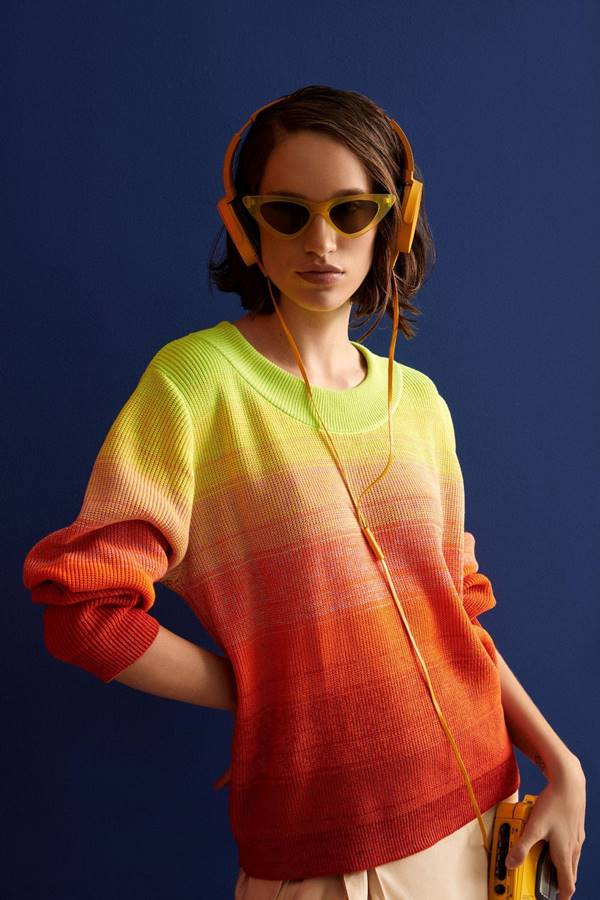 Usando suéter colorido de tricô, mulher de óculos escuros escutando música em fones de ouvido - Metrópoles