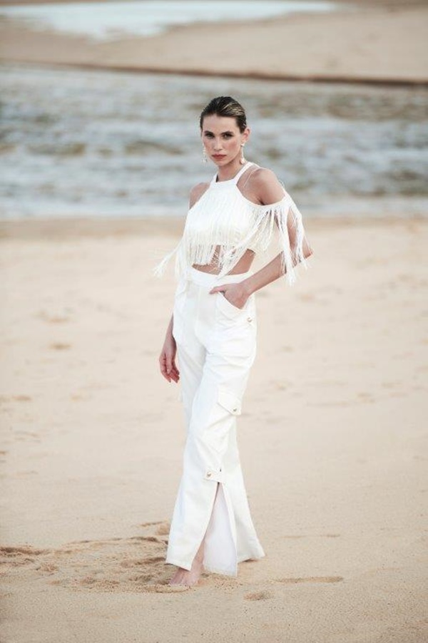 Na praia, mulher usa look branco, formado por top com franjas e calça - Metrópoles