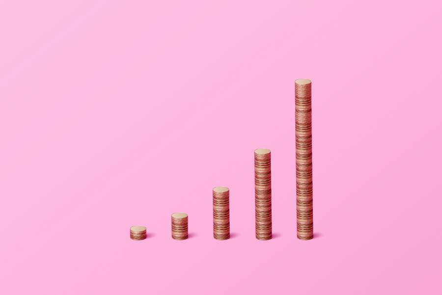 Foto de cinco fileiras de moedas empilhadas de tamanhos diferentes em um fundo rosa - Metrópoles