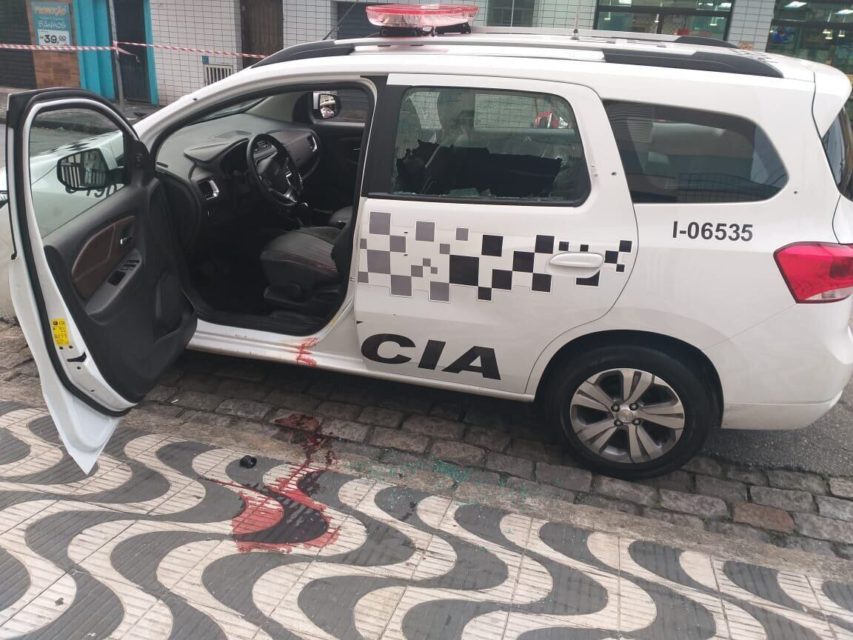 Imagem colorida de viatura da PM com a porrta aberta e sangue de policial na calçada - Metrópoles