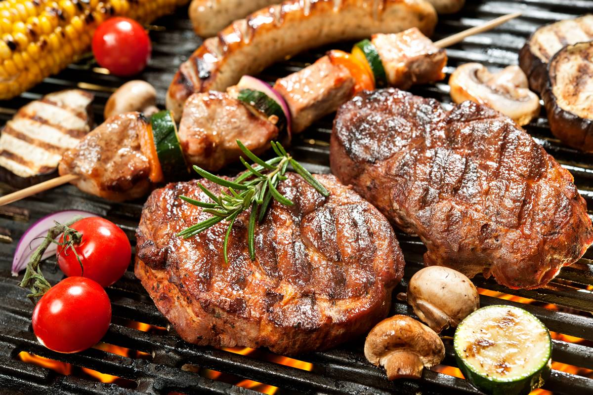 Foto colorida de bifes de carne, espetos de carne, milhos, cogumelos, linguiças em uma grelha - Metrópoles