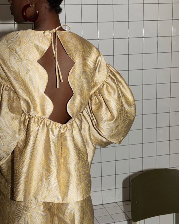 Na imagem com cor, mulher negra possa de costa com vestido dourado - Metrópoles